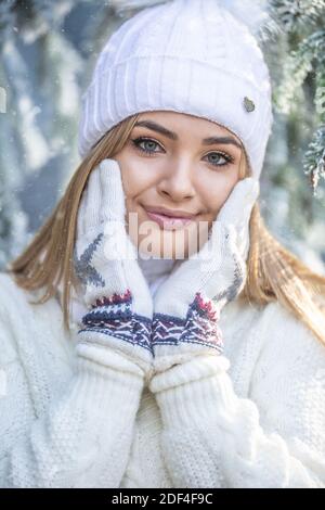 Belle-fille touche sa peau douce de visage avec des gants d'hiver, vêtu d'un pull et d'un bonnet. Banque D'Images