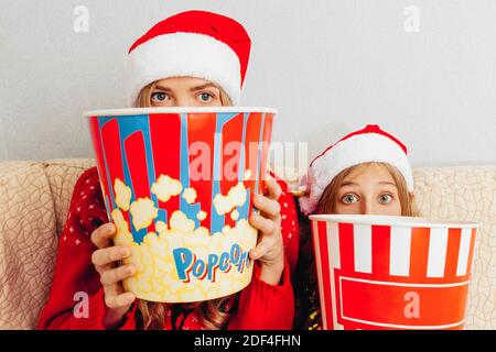 La mère et sa petite fille, vêtues de chapeaux du Père Noël, regardent des films et mangent du pop-corn, assis sur le canapé. Concept de Noël Banque D'Images