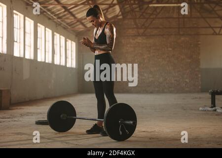 Athlète féminine forte debout avec une barbell sur le sol. Une athlète féminine se prépare à lever le barbell dans un ancien entrepôt. Banque D'Images