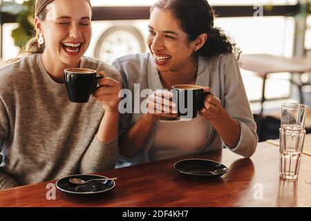 Bonne femme amis dans un café ayant un café. Deux femmes assises à une table basse parlant et riant. Banque D'Images