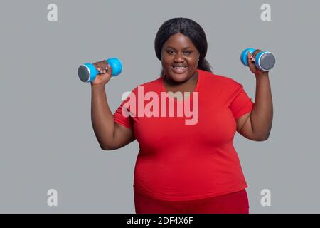 Jeune femme à la peau sombre avec des haltères qui ont l'air excitées Banque D'Images