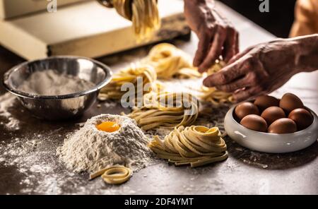 Mains d'un chef tordant des pâtes de fettuccine dans des nids après avoir fait une pâte fraîche à partir des ingrédients. Banque D'Images