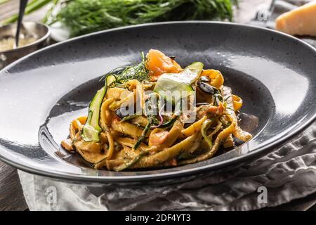 Pâtes linguine au saumon fumé, courgettes, graines de citrouille et fenouil frais servies sur une assiette sombre. Banque D'Images