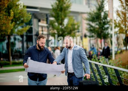 Deux jeunes ingénieurs qui vérifient le plan architectural à l'extérieur Banque D'Images