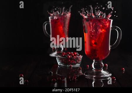 Thé aux baies rouges avec éclaboussures dans deux verres verre à vin avec baie mûre dans un intérieur noir élégant et sombre, espace copie. Banque D'Images