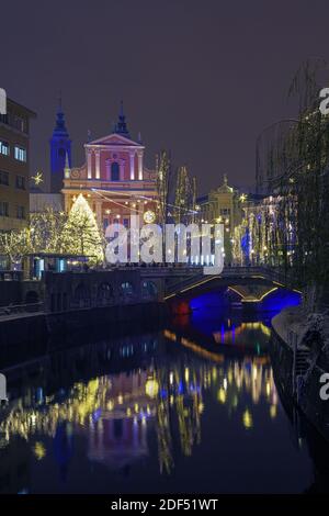 Ljubljana, Slovénie - 2 décembre 2020 : rives enneigées de la rivière Ljubljana, pont triple, sapin de Noël illuminé et église franciscaine Banque D'Images