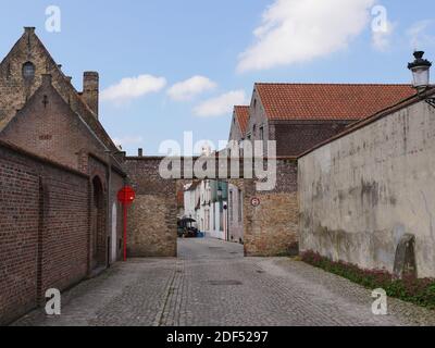 BRUGES, BELGIQUE - 10 mai 2019: Belgique, Bruges , 10 mai 2019, 13:56, rue pavée, droite un mur en béton, gauche un mur et des maisons en briques dans le TH Banque D'Images