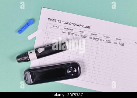 Journal de glycémie pour le diabète avec glucomètre, lancettes, bandes de tests et dispositif de lancing sur fond vert Banque D'Images