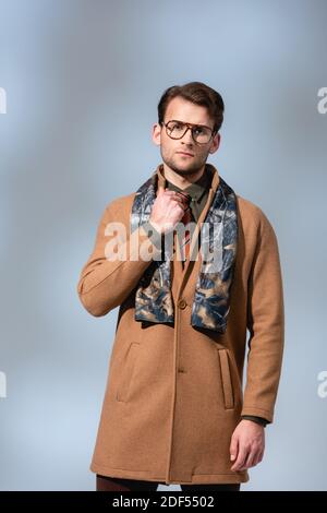 homme tendance en lunettes et manteau d'hiver debout sur le gris Banque D'Images