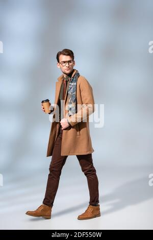 homme élégant en manteau d'hiver tenant le café pour aller et marcher sur le gris Banque D'Images