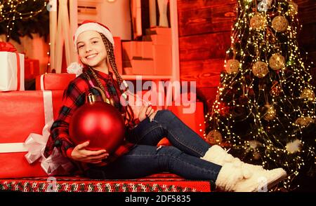 Concept de Noël. Fantaisie enfant santa profitez de la nouvelle année de célébration. Boutique de décoration. Couleur préférée. Style rouge. Répandre l'amour. Maison de vacances d'hiver. Petite fille mignonne avec big ball arbre de Noël. Esprit de Noël. Banque D'Images