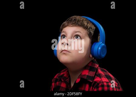 Gros plan sur le visage de l'adolescent dans une chemise rouge à carreaux ecouter de la musique avec un casque circum-aural sans fil bleu arrière-plan noir isolé Banque D'Images