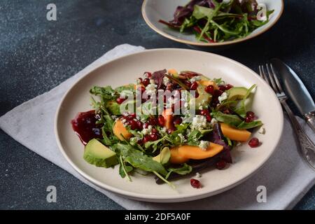 Salade saine persimmon, fromage bleu, épinards, arugula, feuilles de laitue sur plaque blanche Banque D'Images