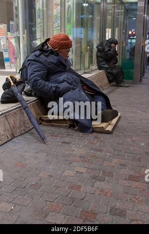 Des hommes sans abri assis près d'une fenêtre de magasin essayant de dormir à Shibuya, Tokyo, Japon Banque D'Images