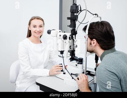 Optométriste femme regardant la caméra lors de l'examen oculaire d'un patient masculin avec un équipement ophtalmique spécial. Profession d'ophtalmologiste Banque D'Images