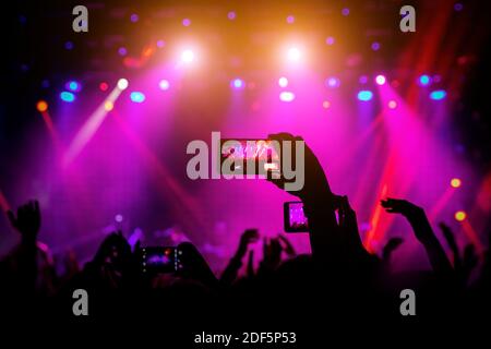 Smartphone à portée de main lors d'un concert, lumière rouge de la scène Banque D'Images