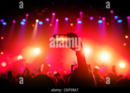 Smartphone à portée de main lors d'un concert, lumière rouge de la scène Banque D'Images