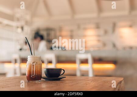 Verre glacé latte avec latte dans une tasse sombre sur une table en bois dans le restaurant et le café-restaurant arrière-plan flou, espace de copie pour le texte Banque D'Images