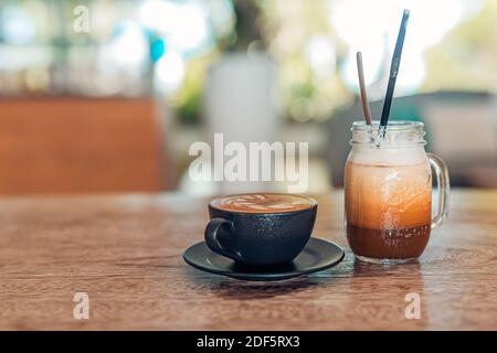 Verre glacé latte avec latte dans une tasse sombre sur une table en bois dans le restaurant et le café-restaurant arrière-plan flou, espace de copie pour le texte Banque D'Images