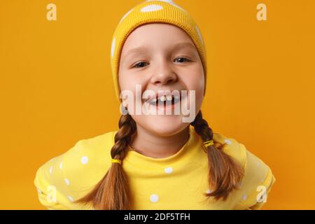 Drôle petite fille mignonne dans un chapeau et avec des picots sur un fond jaune. Banque D'Images