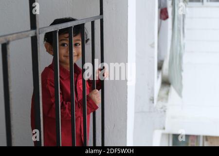 Portrait d'Indien mignon petit gai brune petit garçon tamoul porter une chemise rouge vif tout en étant debout sur un balcon à l'intérieur un fond urbain blanc Banque D'Images