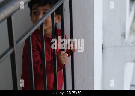 Portrait d'Indien mignon petit gai brune petit garçon tamoul porter une chemise rouge vif tout en étant debout sur un balcon à l'intérieur un fond urbain blanc Banque D'Images