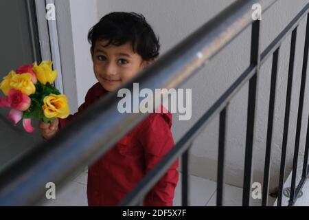 Portrait d'Indien mignon petit gai brune petit garçon tamoul porter une chemise rouge vif tout en étant debout sur un balcon à l'intérieur un fond urbain blanc Banque D'Images