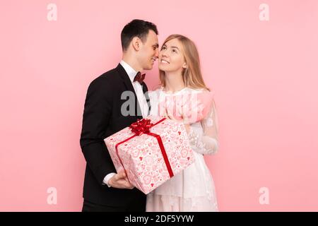 Un couple affectueux, un homme donne à une femme un bouquet de tulipes et une boîte avec un cadeau sur fond rose. Saint Valentin Banque D'Images