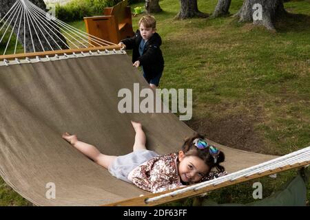 Une fille de trois ans joue sur un hamac alors que son frère, 6 ans, la roque.