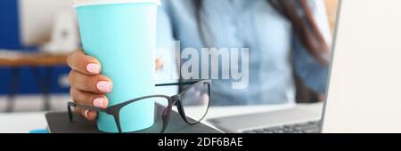 La main féminine tient une tasse de café sur le lieu de travail. Banque D'Images