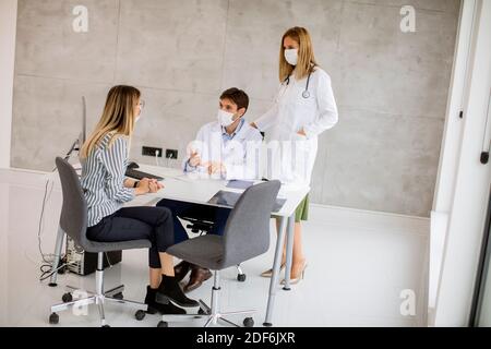 Couple médical médecins avec masques médicaux de protection du visage parler avec jeune femme et l'utilisation de l'ordinateur dans l'offic Banque D'Images
