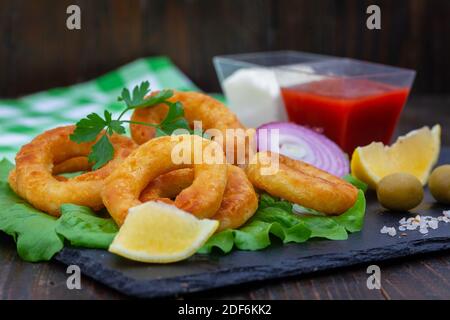 Hors-d'œuvre de calmars ou de rondelles de poisson frits. Calmars panés ou rondelles de poisson avec citron, ketchup et mayonnaise. En-cas calamars doré et croquant sur le boa noir Banque D'Images