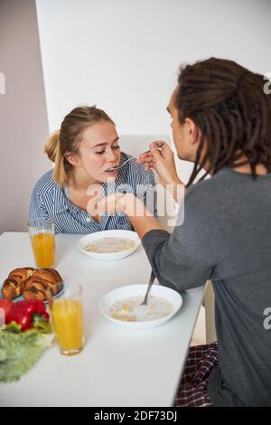 Jeune homme aimant nourrissant une petite amie avec une cuillère dans la cuisine Banque D'Images