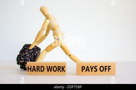 Symbole travail dur. Blocs en bois avec les mots « dur labeur rapporte ». Modèle en bois de l'homme avec pierre noire. Magnifique arrière-plan blanc, espace de copie. Bus Banque D'Images