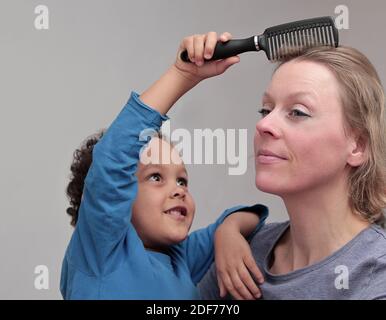 enfant jouant à la coiffure avec la mère sur fond gris stock photo Banque D'Images