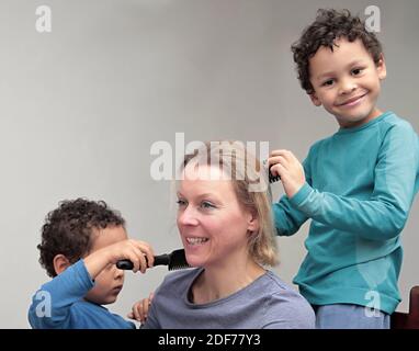 enfant jouant à la coiffure avec la mère sur fond gris stock photo Banque D'Images