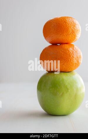 deux oranges empilées sur une pomme verte comme un joueur bonhomme de neige aux fruits avec espace de copie sur fond blanc Banque D'Images