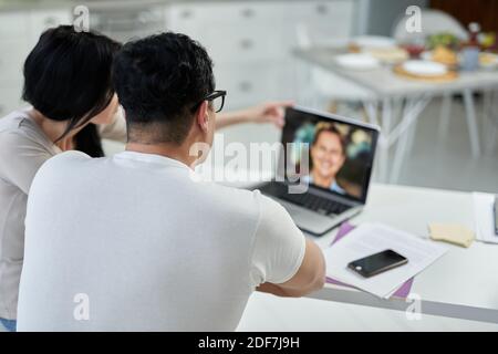 Vue arrière d'un couple hispanique d'âge moyen, d'un homme et d'une femme communiquant avec un tuteur pendant un cours de formation en ligne tout en étudiant à distance, à l'aide d'un ordinateur portable à la maison. Éducation à distance pour adultes Banque D'Images