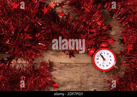 Compter les derniers instants avant Noël ou le nouvel an. Compte à rebours jusqu'à minuit. Réveil rouge allongé sur une table dans une guirlande lumineuse et scintillant en gros plan. Banque D'Images