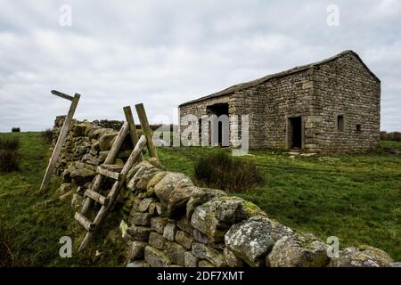 Ancienne grange en pierre tortueuse avec pilotis en bois et panneau de chemin de pied près de Hebden et Burnsall, parc national de Yorkshire Dales, North Yorkshire, Angleterre, Royaume-Uni Banque D'Images