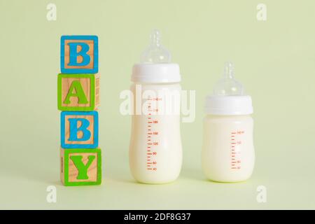 Un « Baby » écrit en bois à côté de bouteilles pleines de lait sur fond vert pastel Banque D'Images