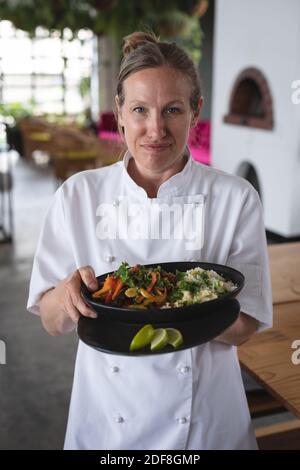 Portrait d'une femme chef caucasienne tenant un bol de plat de riz et de salade dans la cuisine du restaurant Banque D'Images