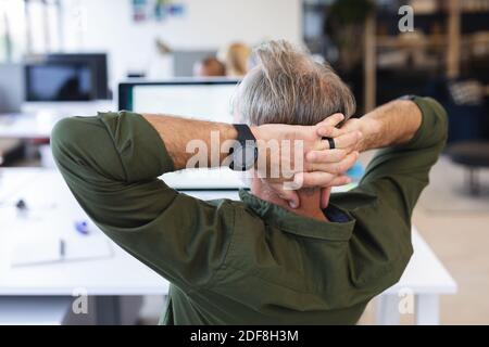 Vue arrière de l'homme caucasien dans le bureau créatif de repos, mains sur la tête Banque D'Images