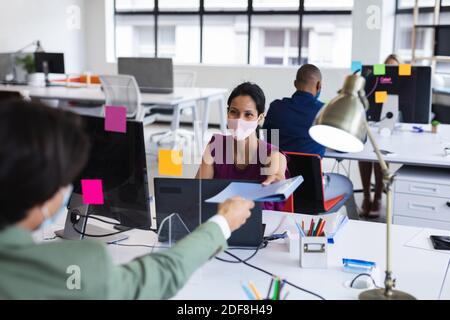 Divers hommes et femmes portant des masques faciaux transmettant des documents bureau Banque D'Images