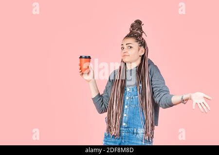 Élégante et belle jeune femme avec des queues de cochon afro tient une tasse jetable de café en papier. Surprise sur le visage et les bras se répandent. Concept pour la publicité des boissons Banque D'Images