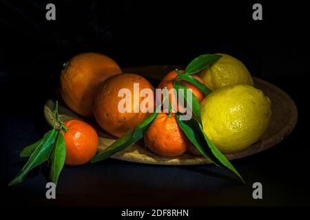 Vitamine C. Plateau en bois avec agrumes. Deux citrons jaunes, deux oranges et trois mandarines aux feuilles vertes. Banque D'Images