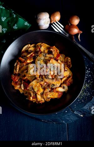 Champignons cuits aux herbes et épices dans une assiette noire. Saute de champignons. Banque D'Images