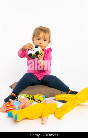 Une petite fille joue avec des jouets pour garçons et regarde l'appareil photo. Stéréotypes de genre. Banque D'Images