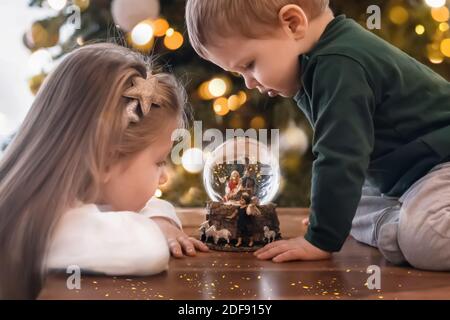 Sœur et frère regardant une boule de verre avec un Scène de la naissance de Jésus-Christ dans un verre Boule sur un arbre de Noël Banque D'Images