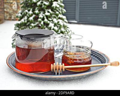 Bouilloire en verre de thé chaud et pot de miel sur table recouverte de neige. Sapin caucasien sur fond. Gros plan avec l'espace de copie. Banque D'Images